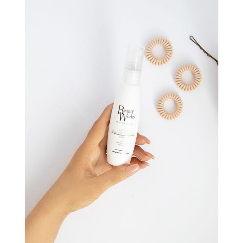 Model holding Beauty Works Heat Protection Spray, travel size